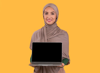 Muslim Woman Showing Blank Laptop Screen Over Yellow Studio Background