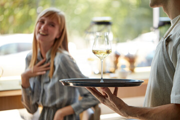 glad waiter bring glass of champagne on tray to customers, treats women in restaurant. caucasian woman is thankful for service. focus on glass with beverage