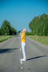 A young albino woman in yellow, standing on the road, holding a bouquet of daisies. against the blue sky.