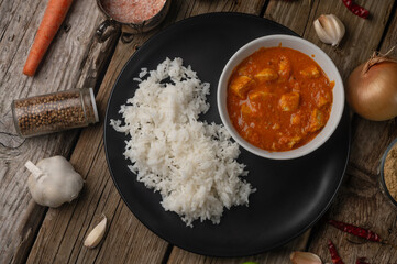 Plate with classic chicken curry and rice served with lime and spices on rustic wooden table background. Traditional indian cuisine. Asian recipe.