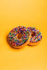 Two of chocolate frosted donuts with sprinkles on yellow background. Playful and joyful tasty sugary comfort food for customers with copy space.