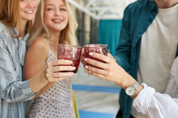 group of young friends clinking glasses with beverages in cafe, they share news, rest after work or celebrate something