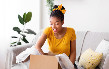 Happy black woman unpacking parcel after online shopping