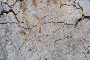 Texture of cracked sandy soil containing small stones, branches and debris