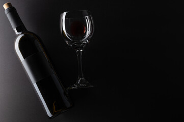 Elegant bottle and wineglass of red wine on black background. Top view. Flat lay. Concept of advertising and promotion of alcoholic drinks. Space for text.
