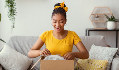 Happy black woman unpacking box after online shopping - obrazy, fototapety, plakaty