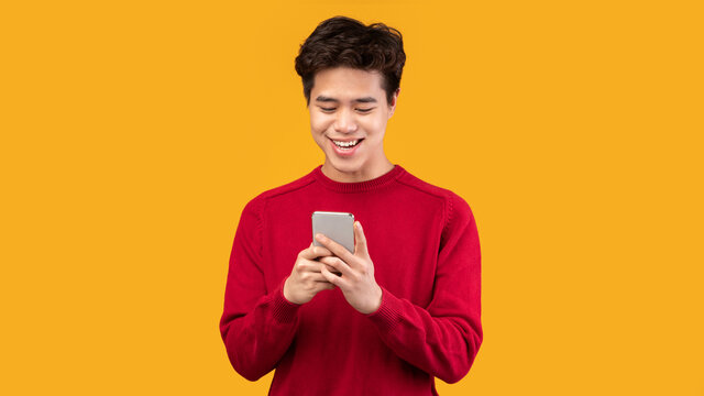Happy Asian Guy Using His Mobile Phone At Studio
