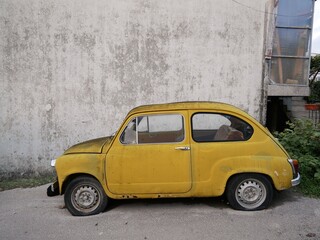 Yellow retro car stands near the grey wall of the house