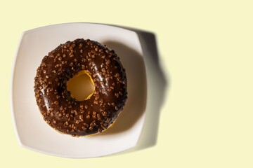 Close up view of chocolate donut  on white plate and yellow background. Food and health concept.