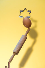 bakery levitation with rolling pin, egg and star shaped cake pan. each ingredient is on top of the other. a finger supporting objects. yellow background