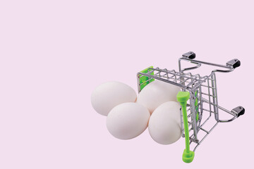 Close up view of shopping cart with white eggs on pink background. Eastern. Food. Shopping.
