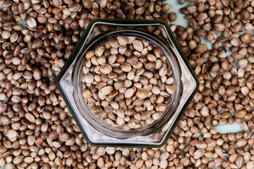 Cannabis seeds in a dark glass bottle isolated on a dark brown tree from above. Spilled hemp.