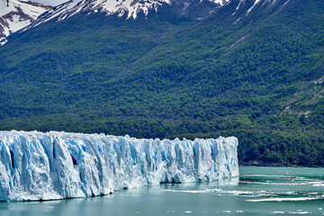 Blue ice of Perito Moreno Glacier in Glaciers national park in Patagonia, Argentina with turquoise water of Lago Argentino in the foreground, dark green forests and sow covered mountains of the Andes