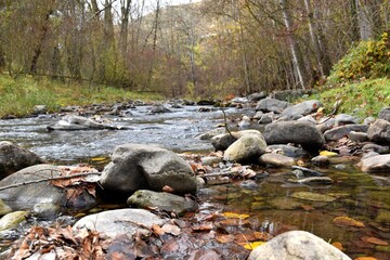 River with stones, water and leaves in autumn.