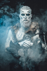 Nordic savage undead in dark armour with white skin and blue eyes holding his huge axe in smokey...