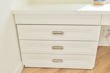 White wooden chest of drawers with vintage bronze handles under desk