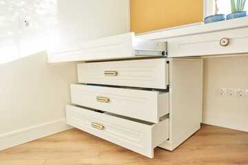 White wooden chest of drawers with vintage bronze handles under desk