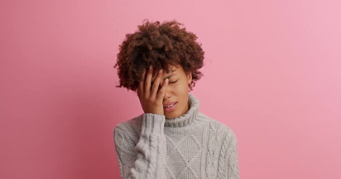 Afro American woman gestures and asks someone demands answer makes face palm with disappointment feels unhappy or frustrated cannot hear what she wants dressed in knitted sweater poses indoor