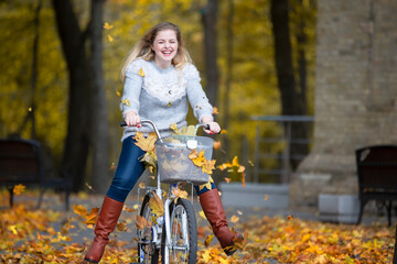 Cheerful woman rides a bicycle in the autumn park. Beautiful autumn background with girl and leaves.