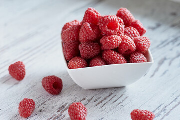 Raspberries in a white bowl on a white wooden table.