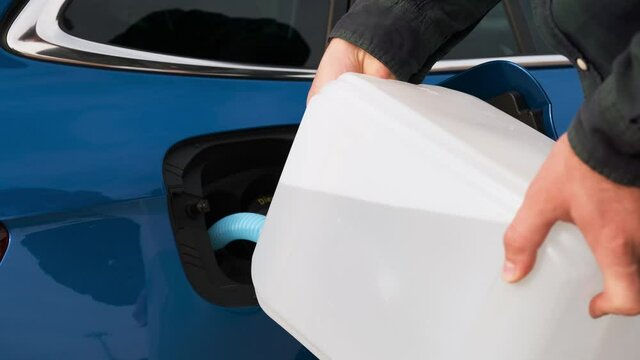 Close up man filling a diesel engine or exhaust fluid DEF from canister into the tank of blue car.