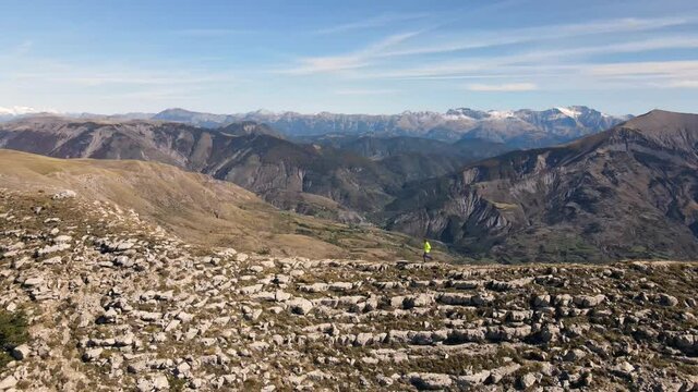 un coureur court avec des b&acirc;tons sur une cr&ecirc;te devant un panorama de montagnes enneig&eacute;es