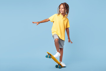 Active little boy with african dreads on skateboard having fun over blue background.