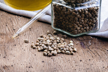 Hemp oil in a glass jug. and marijuana seeds close up on wooden board