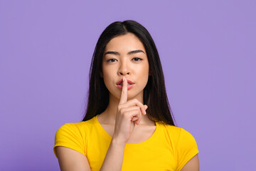 Fototapeta premium Shhh. Mysterious young asian lady showing keep silence sign at camera
