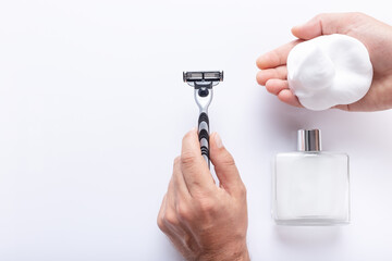 Hands holding razor blade and shaving foam, with after shave isolated on white background, with copy space, top view. Shaving products for men.