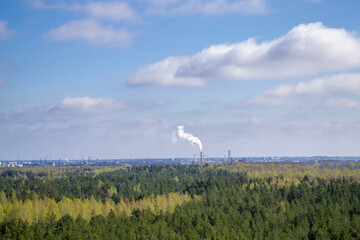Fuming factory chimneys and forest top view. Aerial view to tops of trees and city in the background. Landscape of Riga, Latvia.