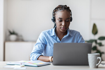 Young black hotline operator female in headset working with laptop in office