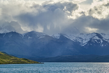 Towers of torres del Paine national park covered in clouds with dark green forest a lake and snow covered mountains of the Andes in Patagonia southern Chile