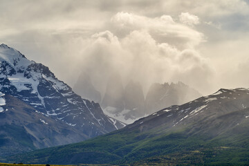 Towers of torres del Paine national park covered in clouds with dark green forest a lake and snow covered mountains of the Andes in Patagonia southern Chile
