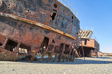 old rusty and rotten ship wreck with holes in its carcass, lying on the beach of the coast line of...
