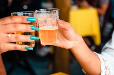 Two girl friends toasting with glasses of light beer on typical brazilian cup (americano long drink).