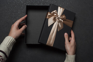 Open gift box with golden ribbon and bow. The guy opens a black gift box