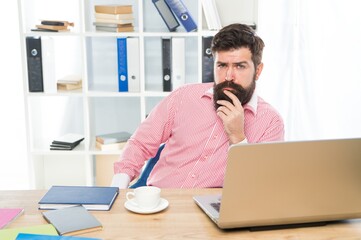 Fototapeta premium Bearded man with serious look sit at managers desktop in modern work room, office