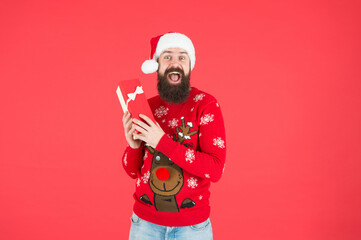 Fototapeta na wymiar happy bearded man hipster wearing funny knitted sweater and santa claus hat and hold present box has an idea for celebrating christmas party, christmas shopping