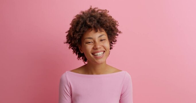 Joyful funny woman hears ridiculous anecdote and laughs out loudly looks cheerful at camera feels carefree or amused dressed in casual clothing isolated on pink wall. Happy emotions concept.