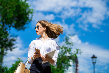 Young beautiful blonde woman in white blouse walking in summer park