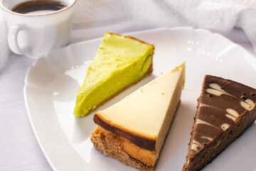 Set of New York, chocolate and pistachio cheesecake on white plate and cup of coffee