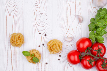 Top view raw tagliatelle pasta with fresh basil, garlic and tomatoes on a rustic white table, flat lay, copy space.