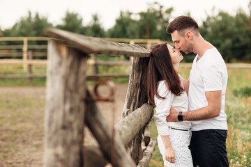 Naklejka na ściany i meble happy couple is kissing near wooden fence. young man and woman are having fun outdoors on a warm summer day.