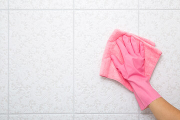 Young woman hand in pink rubber protective glove wiping light gray ceramic tiles with dry rag. Closeup. Spring general or regular cleanup. Empty place for text or logo. Top down view.