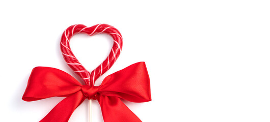 Heart-shaped Lollipop with a bow on a light concrete background. Panorama, top view with space to copy. Concept of holiday backgrounds.