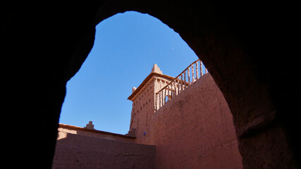 View of the top of a historic Berber kasbah (casbah) through a gate with a tower built of loam and...