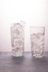 The concept of ice melting. One glass full of ice, the other half full of water. Vertical orientation