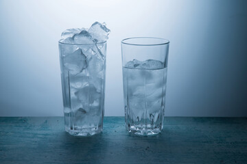 One glass full of ice, the other half full of water.The concept of ice melting. Vertical orientation