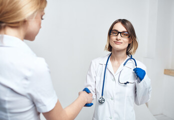 Fototapeta premium The nurse shakes hands with the patient on a light background and blue gloves with a stethoscope